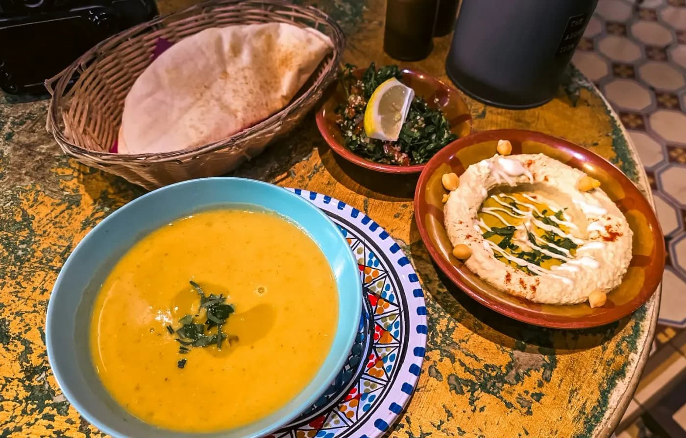 A bowl of soup with bread and hummus on a patterned table